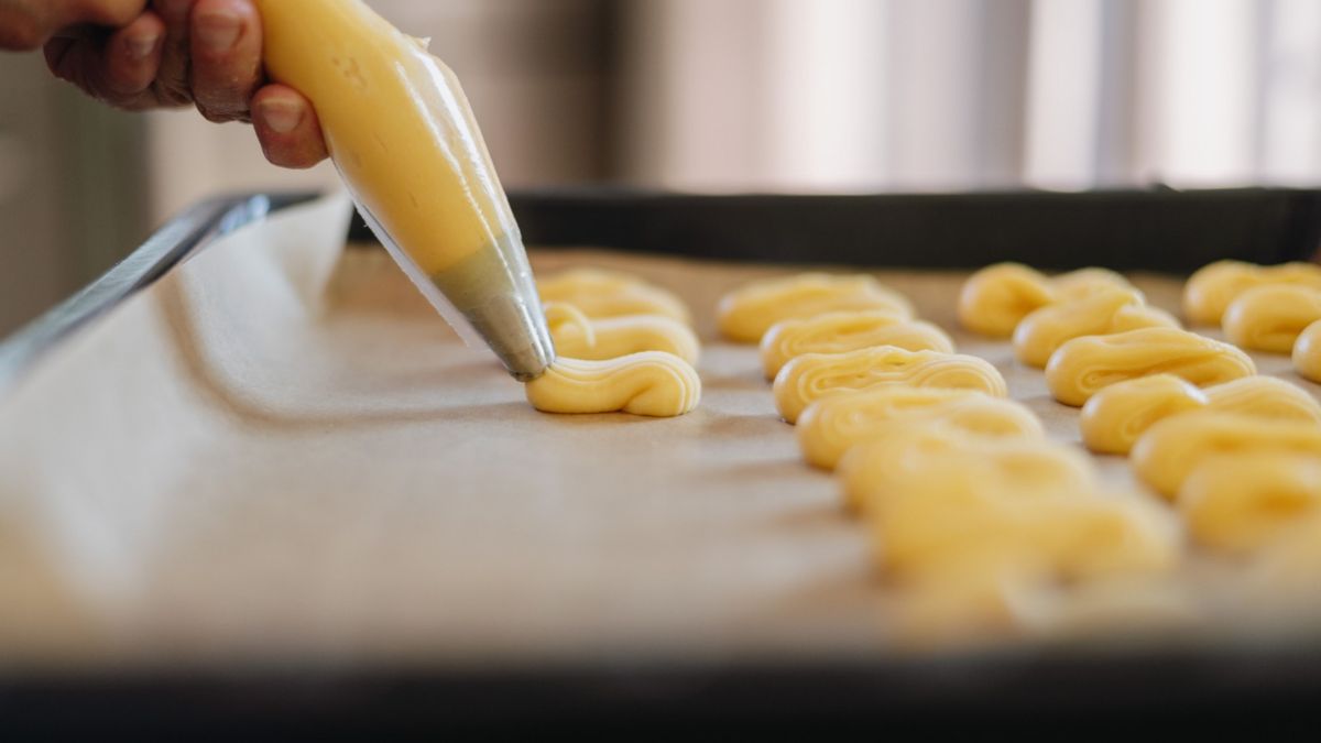 Fertig gebackener Kastenkuchen auf Kuchengitter, dekoriert mit Limettenscheiben. Im Hintergrund eine Person mit Schürze