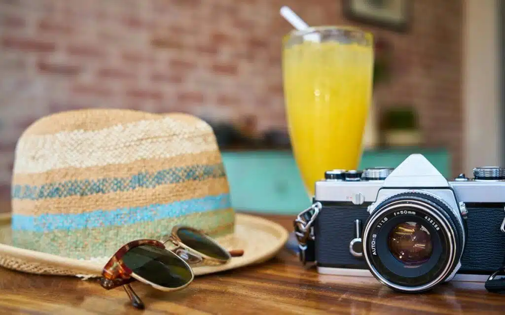 Sonnenhut, Sonnenbrille, Kamera und Cocktail stehen auf einem Holztisch