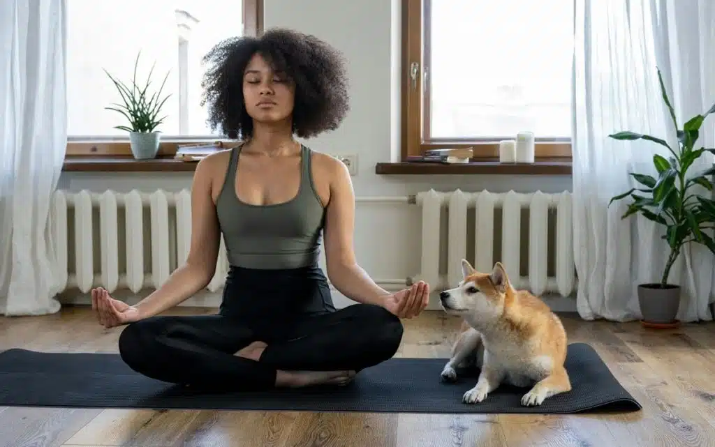 Frau sitzt im Schneiderseitz und mach Yoga, ein Corgi sitzt rechts neben ihr